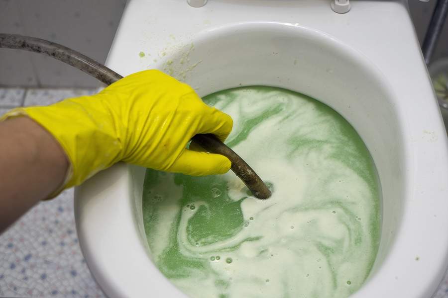 A hand in protective glove fixing clogged toilet.