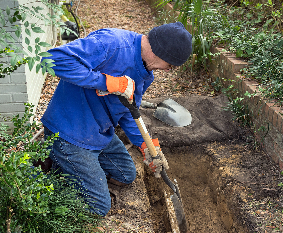 Man digging trench to replace old sewer pipes and lawn sprinkler system line.