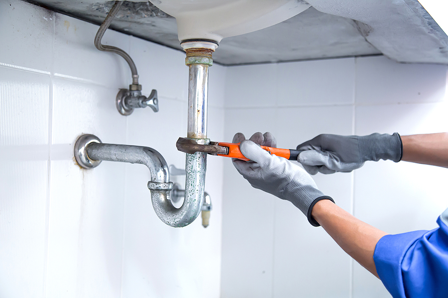 Technician plumber using a wrench to repair a water pipe under the sink.